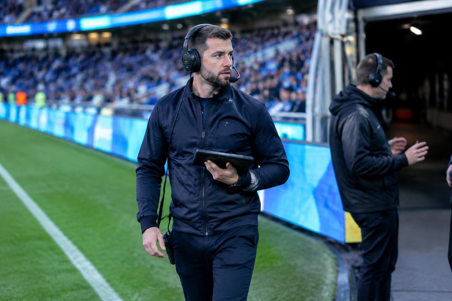 Matchday operations lead with headset and tablet walking pitchside